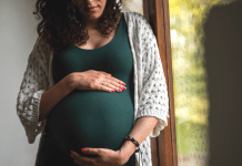 Pregnant Woman by a window holding her stomach motherhood