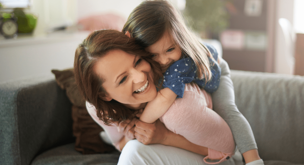 mom with young daughter hugging on a couch
