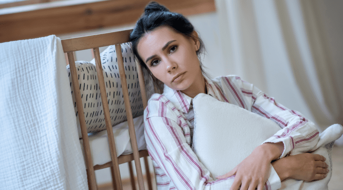 woman comforting self with pillow while leaning against a bed