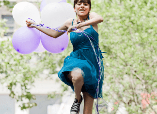 teen girl outside holding balloons and leaping into the air