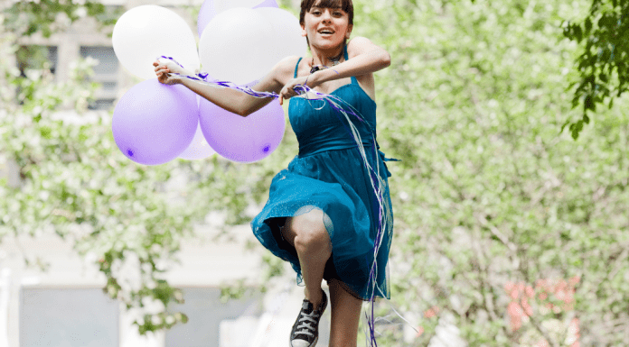 teen girl outside holding balloons and leaping into the air