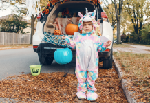 Child in monster costume holding blue pumpkin to collect candy