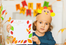 Child wearing a turkey hat made of construction paper holding a thankful craft