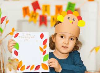 Child wearing a turkey hat made of construction paper holding a thankful craft