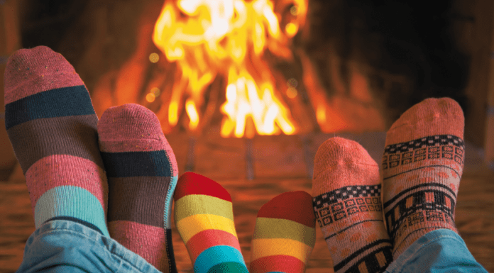 three pairs of feet wearing cozy socks resting in front of a fire in a fireplace.