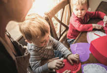 mom and young boys sitting at a table making Valentines out of red and purple construction paper