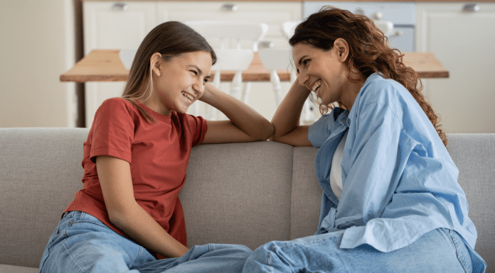 mom and teen daughter sitting on a couch talking to one another and smiling