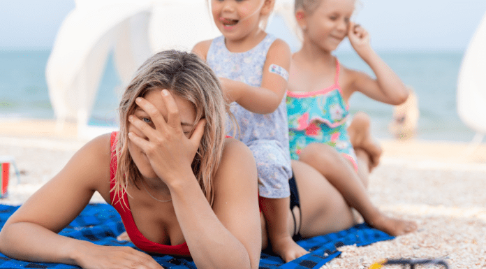 Mom laying on a towel at the beach while her kids sit on her back