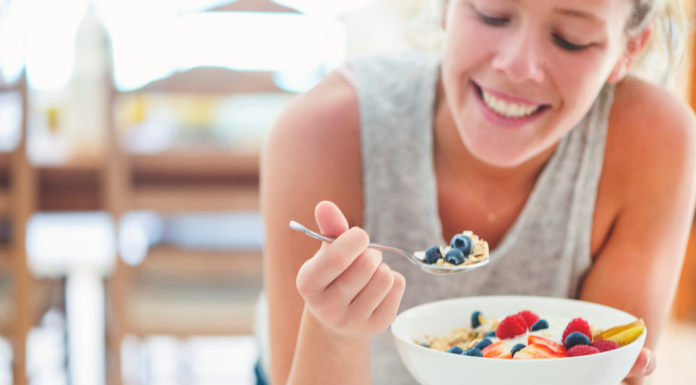 Woman leaning over kitchen counter eating a bowl of fruit.